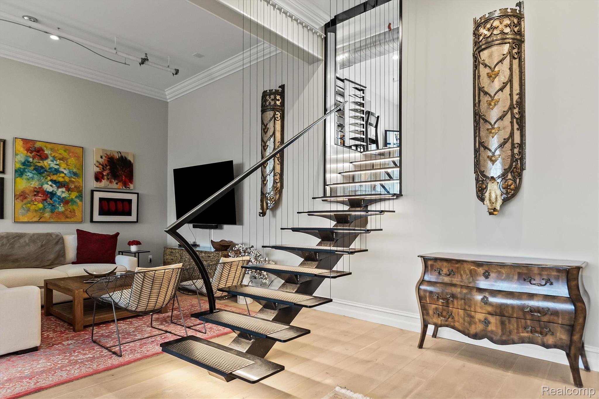 Furnished living room with a striking open staircase and colorful artwork.