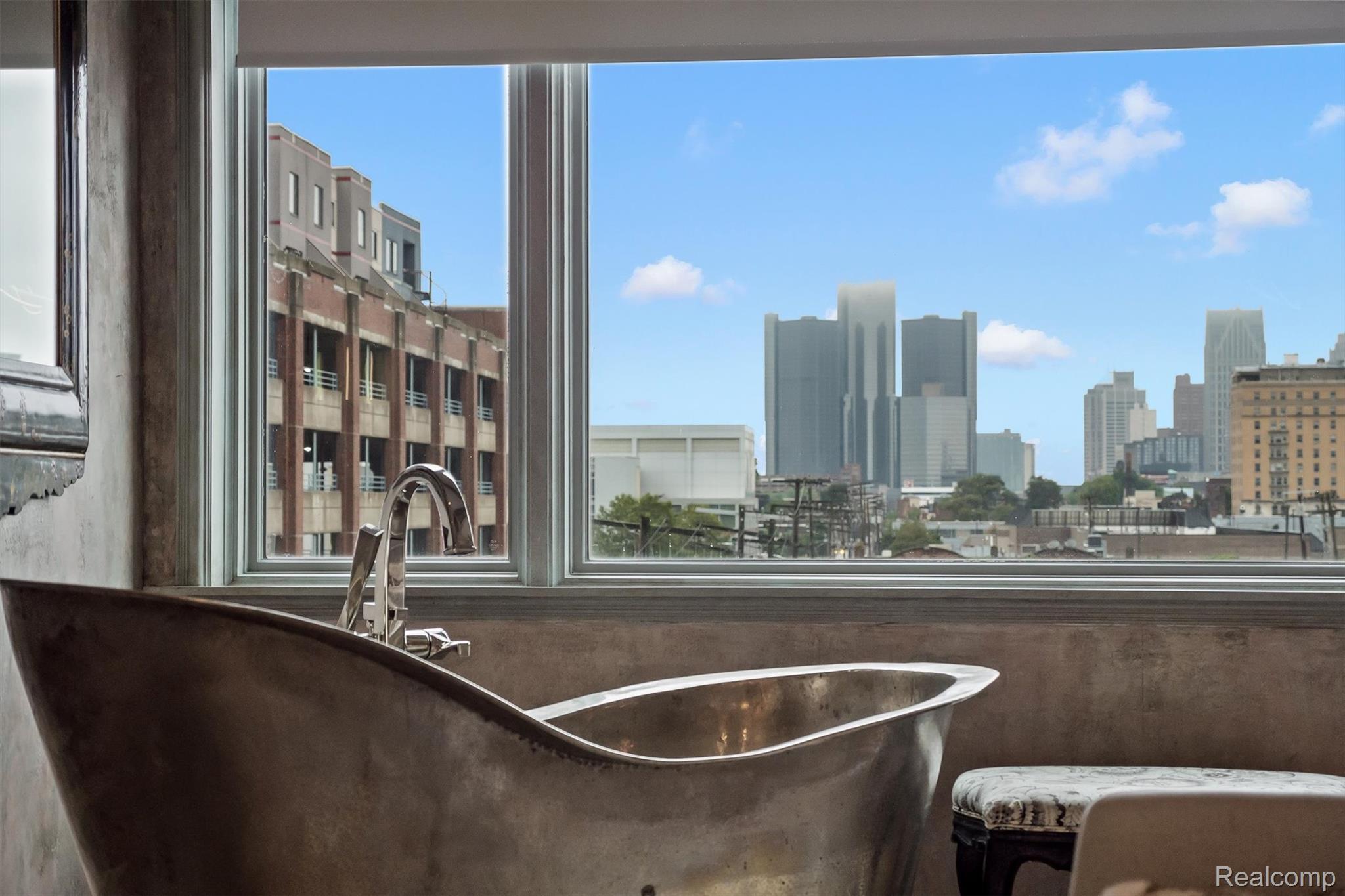 Freestanding bathtub beside a large window overlooking Detroit’s downtown skyline.