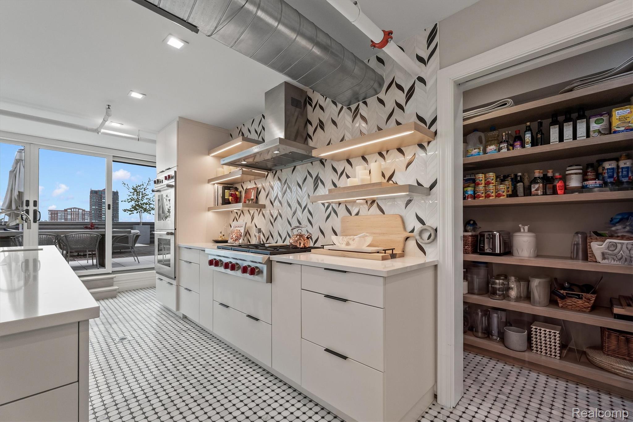 Modern white kitchen with patterned tile, open pantry shelves, and sliding doors to a city-view terrace.