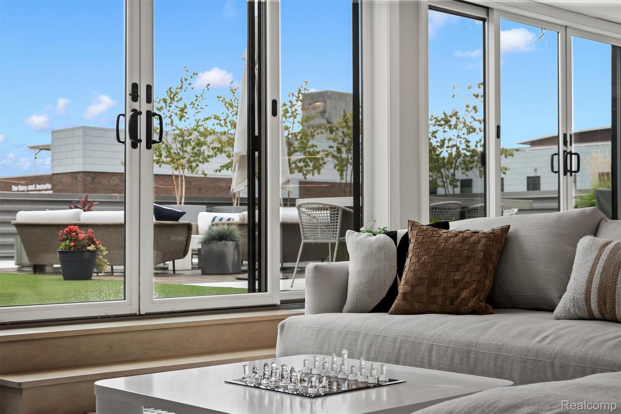 Penthouse living room with a gray sofa and chess set beside glass doors to a furnished terrace.