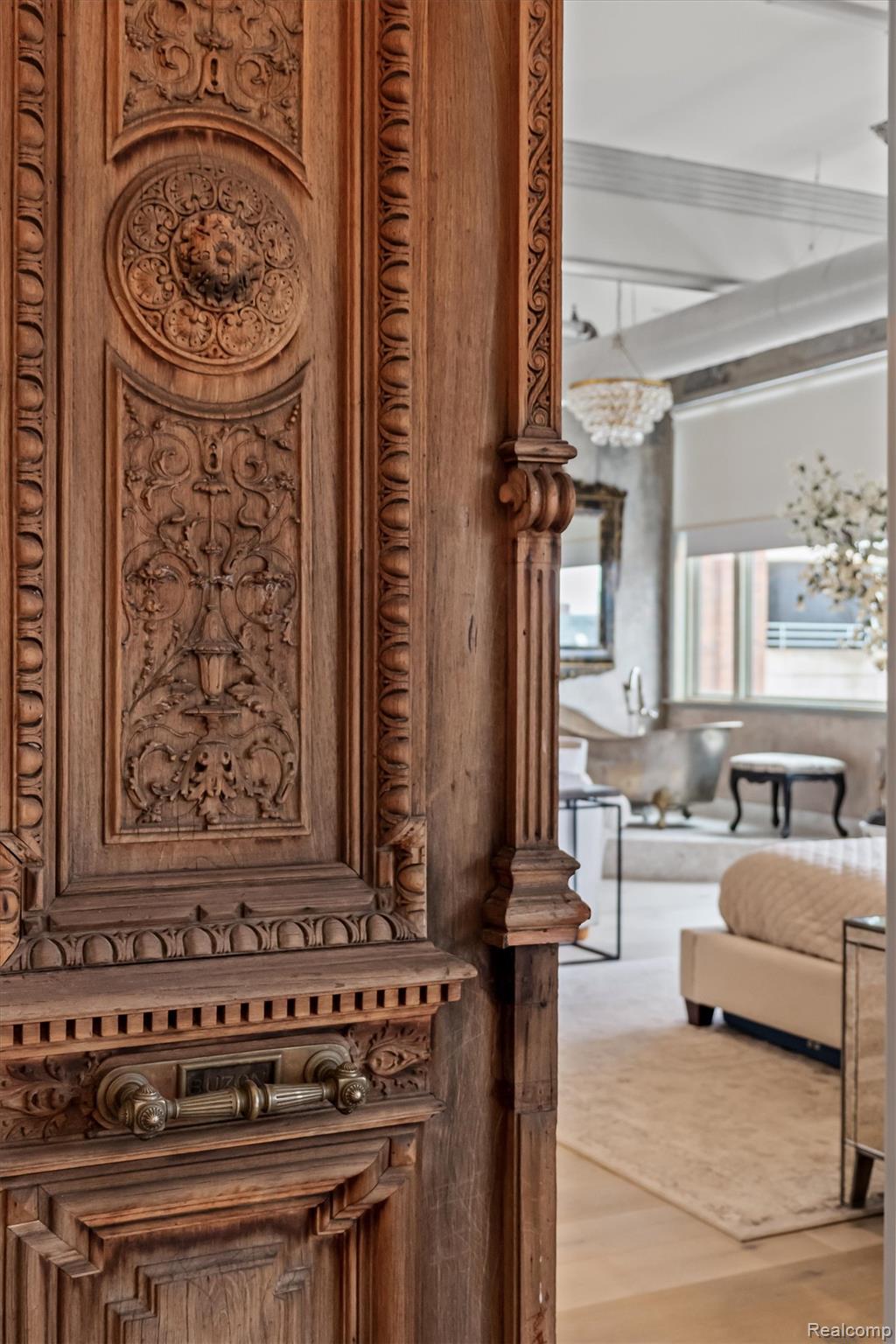 Living room beyond an ornate carved wooden doorway, with a chandelier and neutral furnishings.