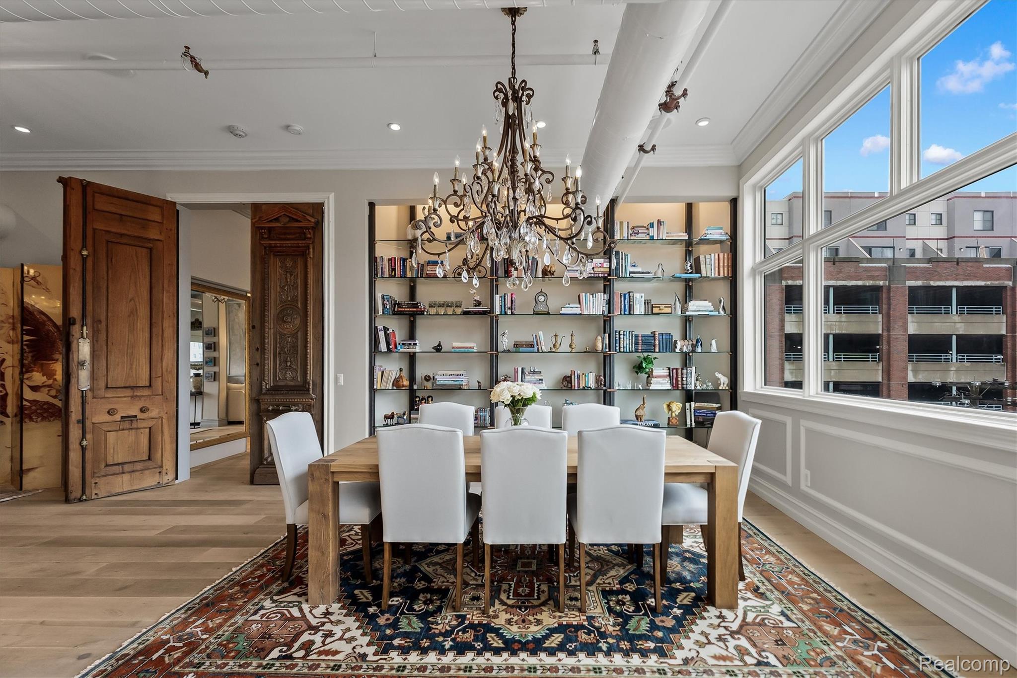 Dining room with an ornate chandelier, built-in bookshelves, carved wooden doors, and large windows.