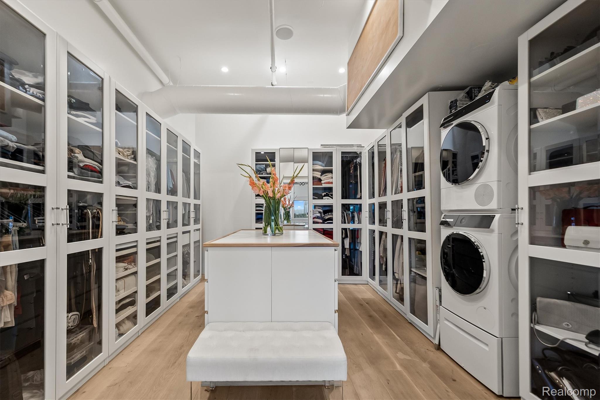 Walk-in closet with glass-front wardrobes, a central island, and stacked washer and dryer.