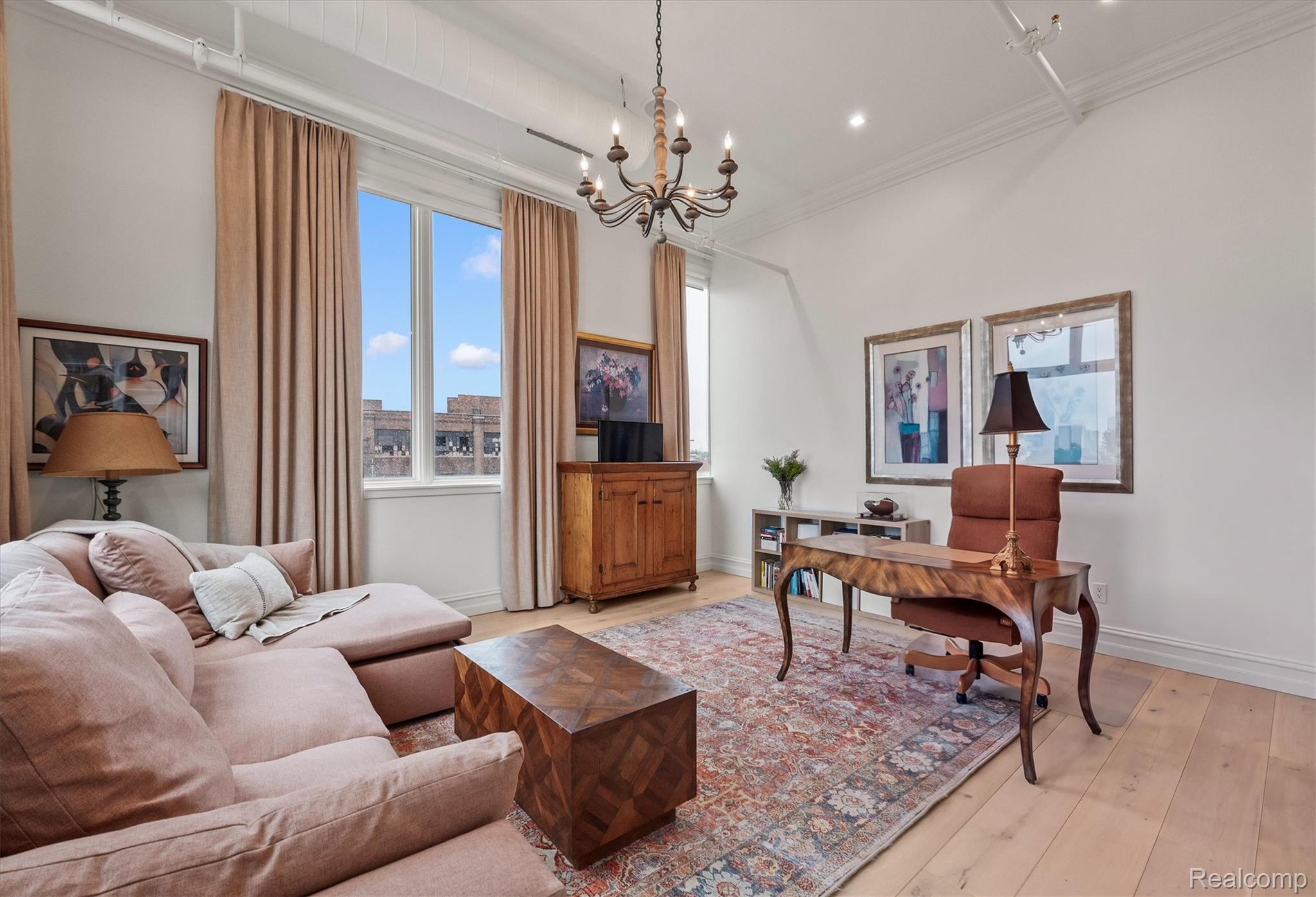 Furnished living room and home office with a pale sectional, carved desk, patterned rug, and tall windows.