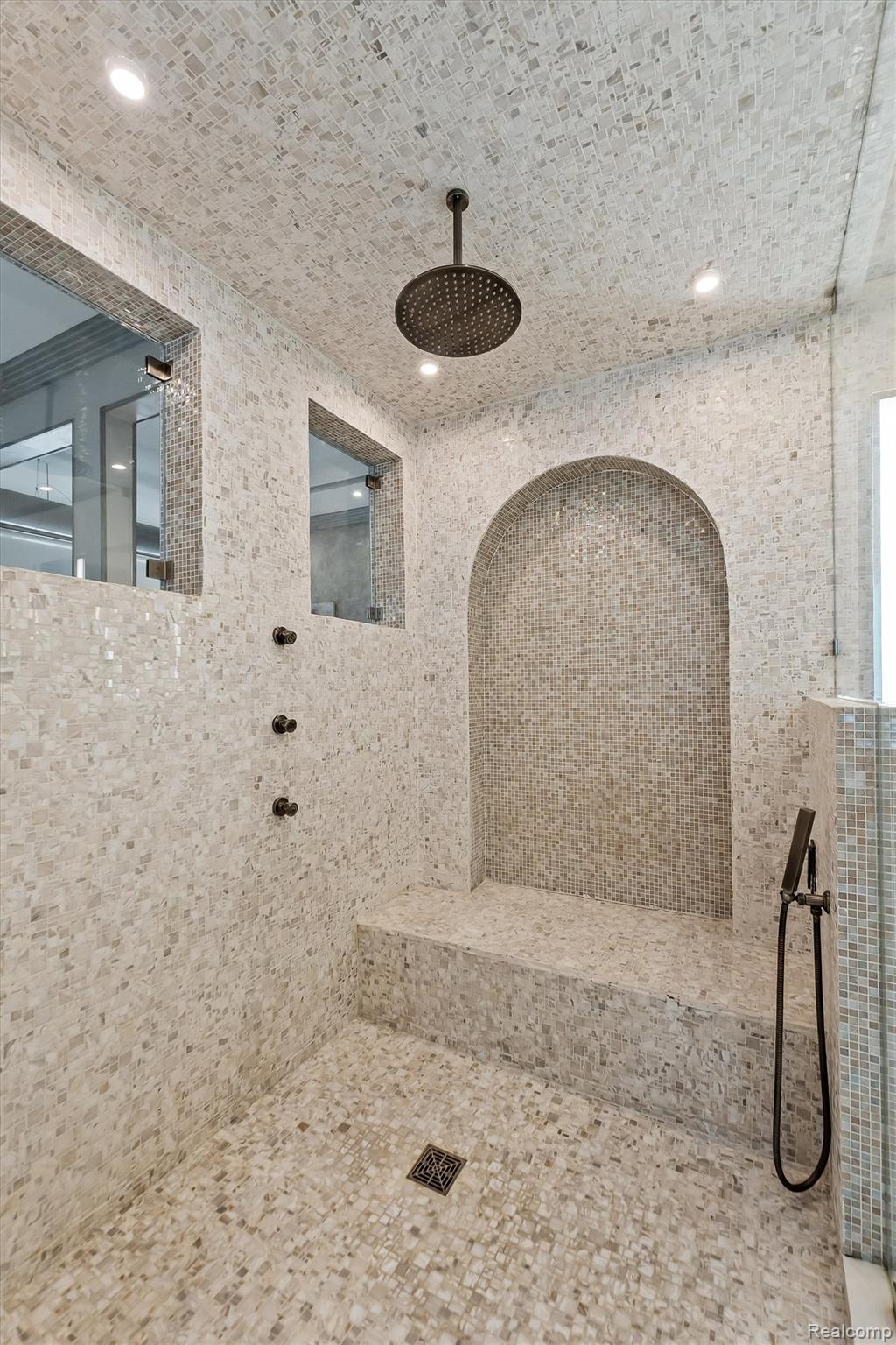 Mosaic-tiled walk-in shower with an arched recessed niche, built-in bench, and overhead rain showerhead.