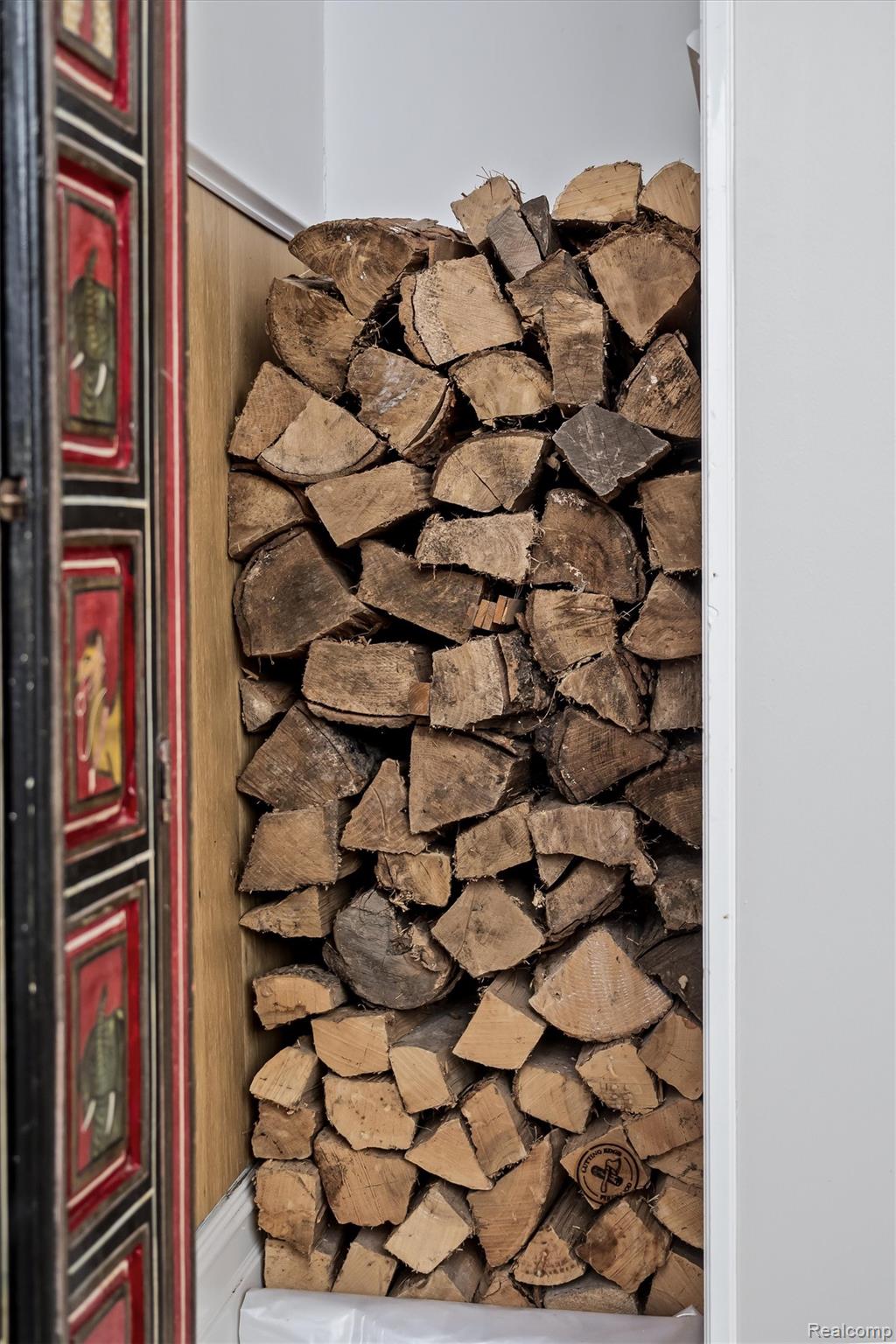 Stacked firewood fills a narrow alcove beside a red-and-black paneled door.