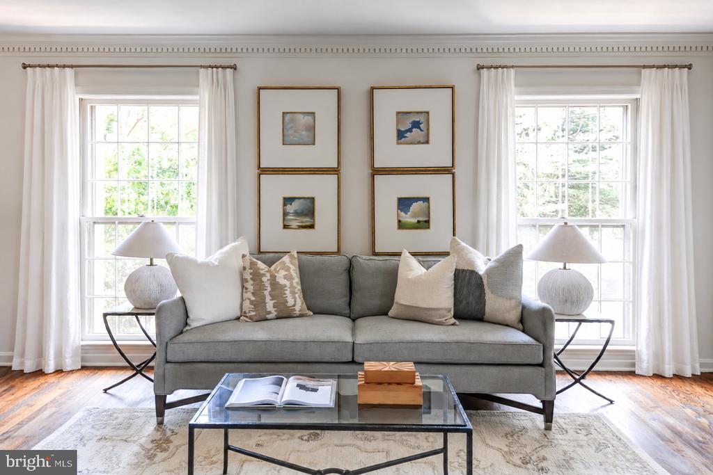 Staged living room with a gray sofa, paired curtained windows, and framed artwork.