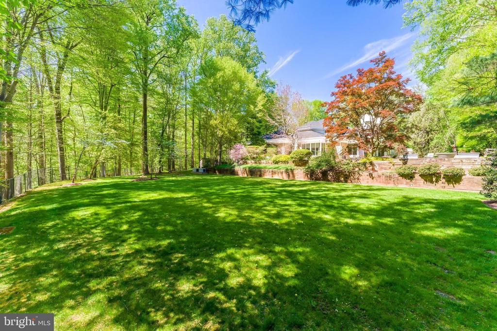 Spacious green backyard framed by mature trees, with the home beyond a brick retaining wall.