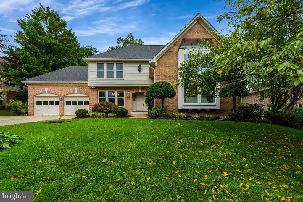 Two-story brick-and-siding home with a two-car garage, broad green lawn, and mature trees.