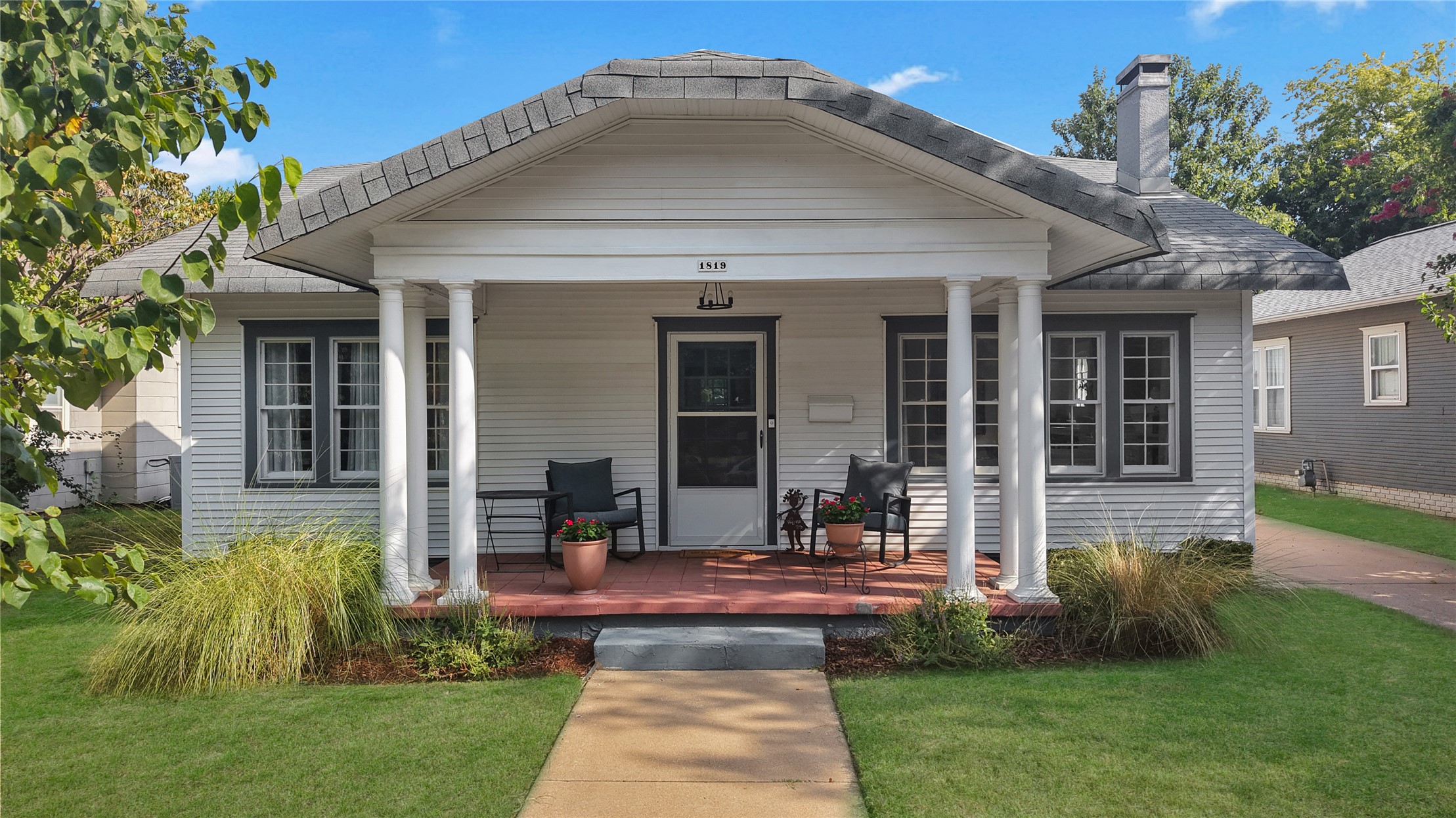 Gray-sided house with a covered porch, white columns, and landscaped front lawn.