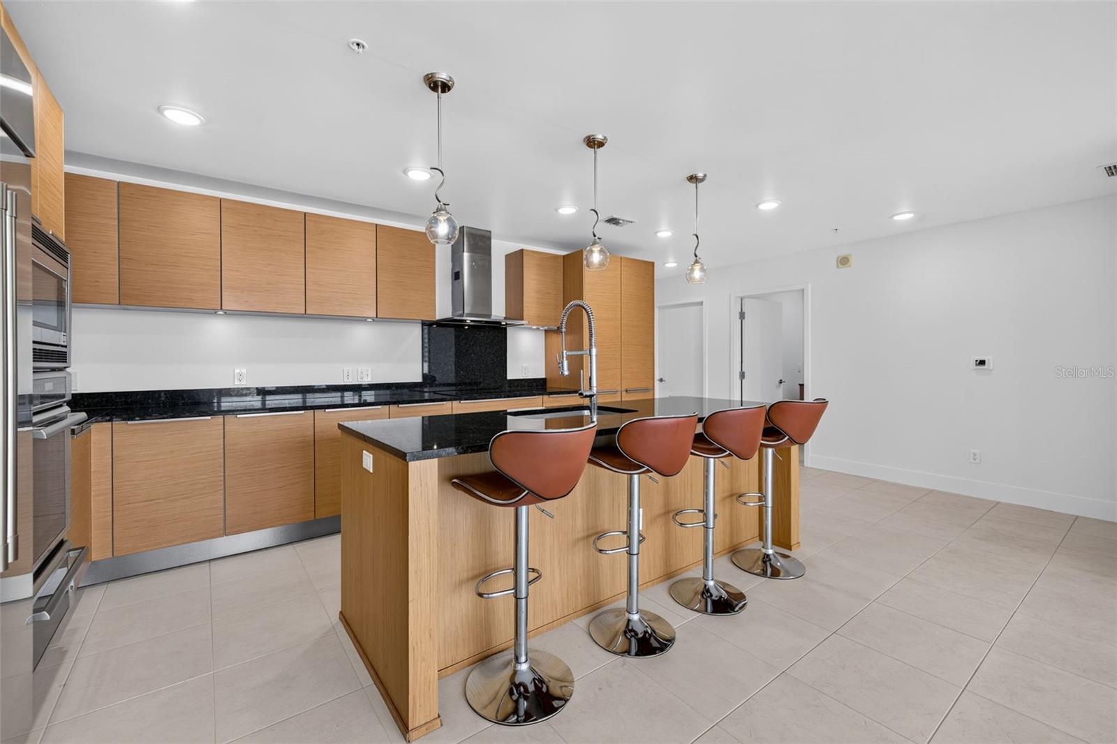 Modern condo kitchen with wood cabinetry, black stone counters, and an island lined with four bar stools.