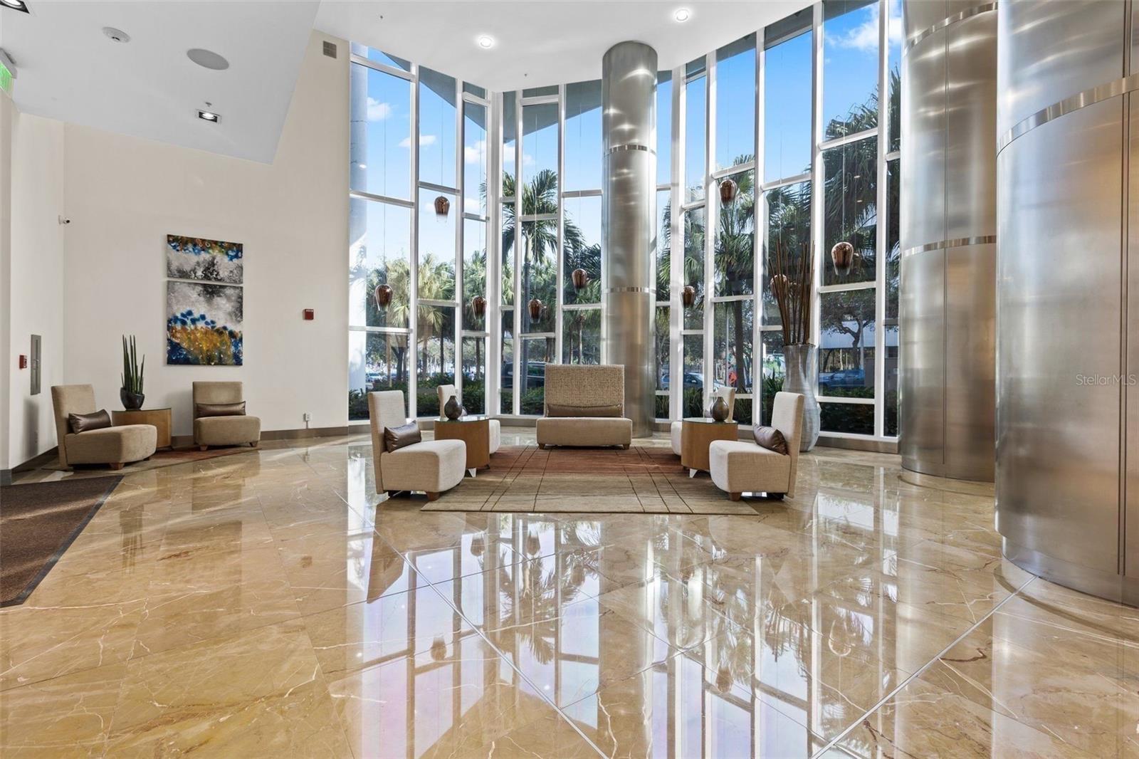 Condominium lobby with floor-to-ceiling windows, marble floors, and modern seating.