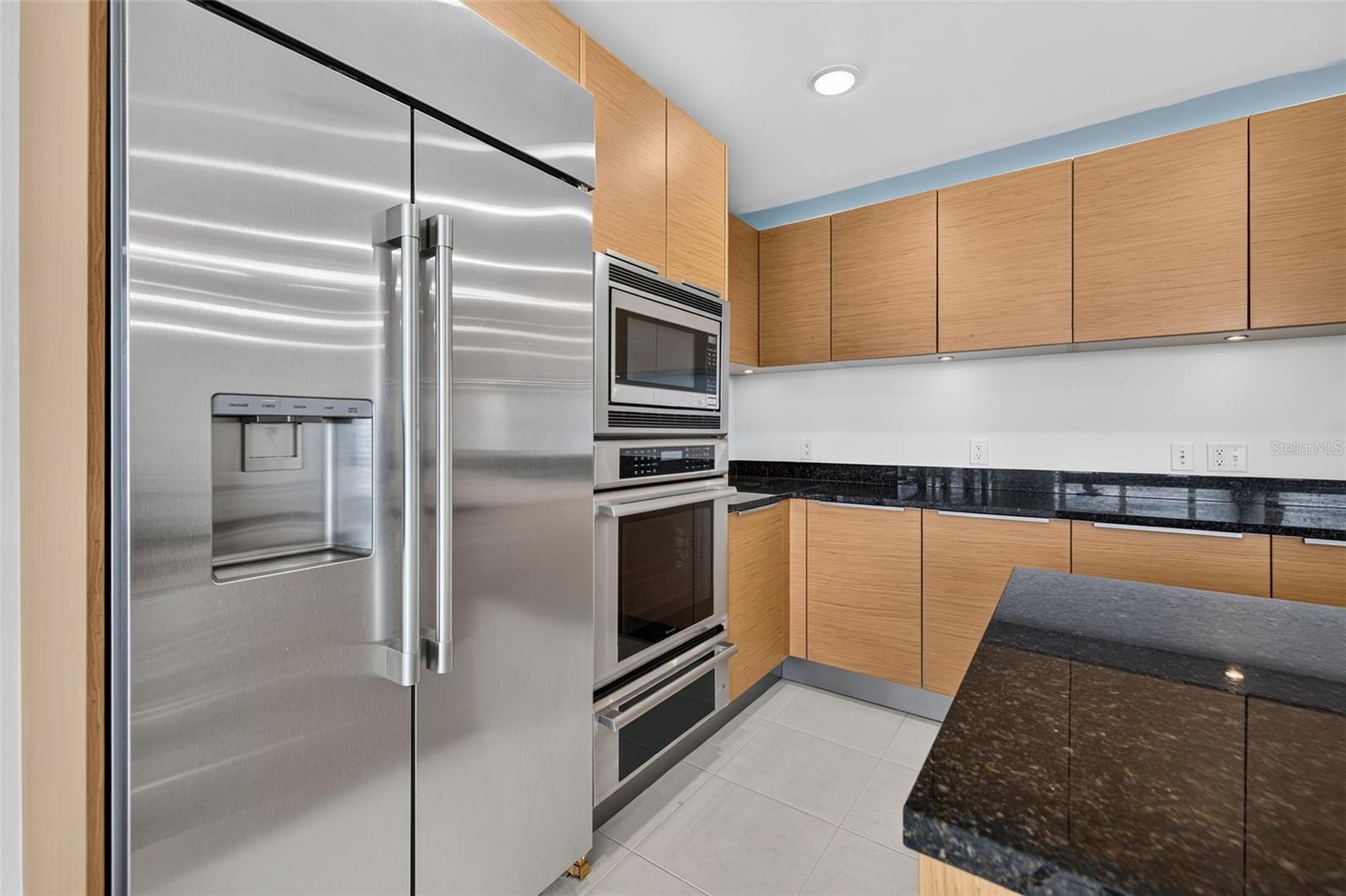 Modern kitchen with light wood cabinets, black stone counters, and stainless steel appliances.