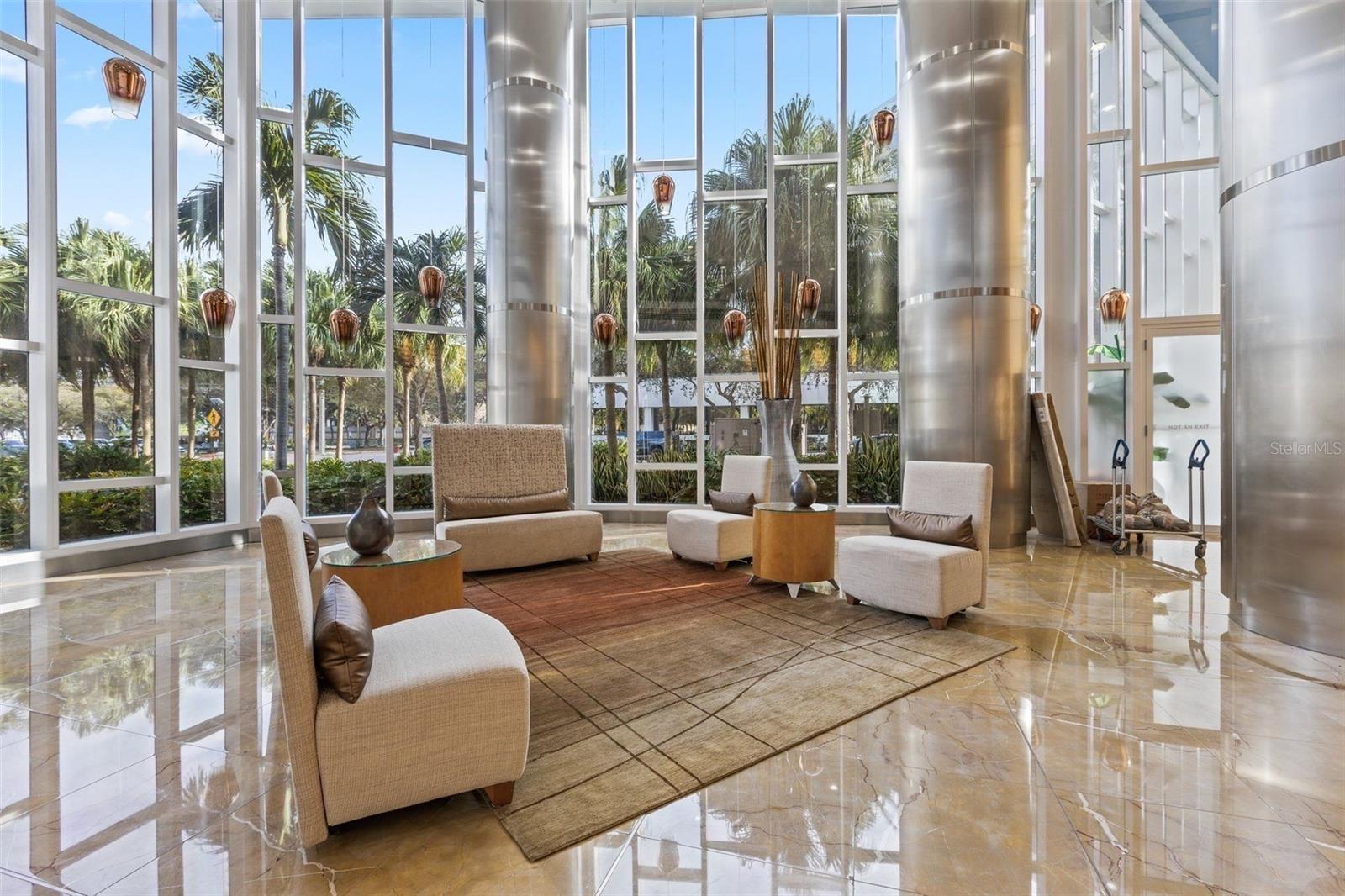 Condominium lobby lounge with beige seating, polished marble floors, tall windows, and metallic columns.