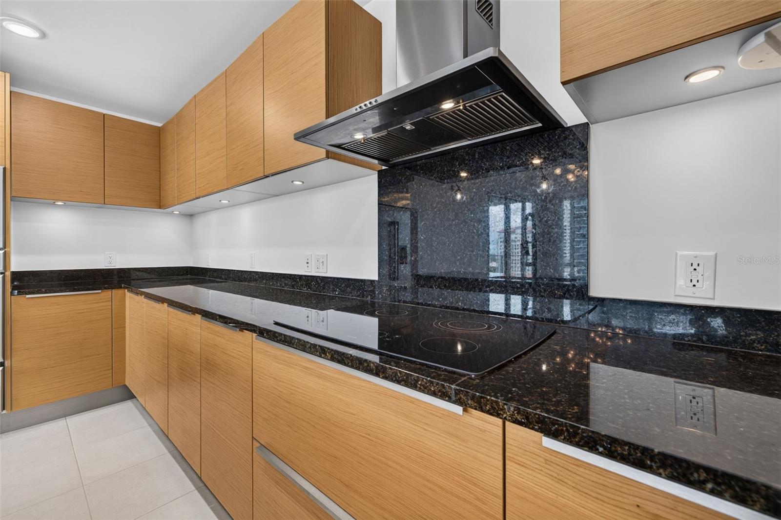 Modern kitchen with light wood cabinets, black stone counters, and a built-in induction cooktop.