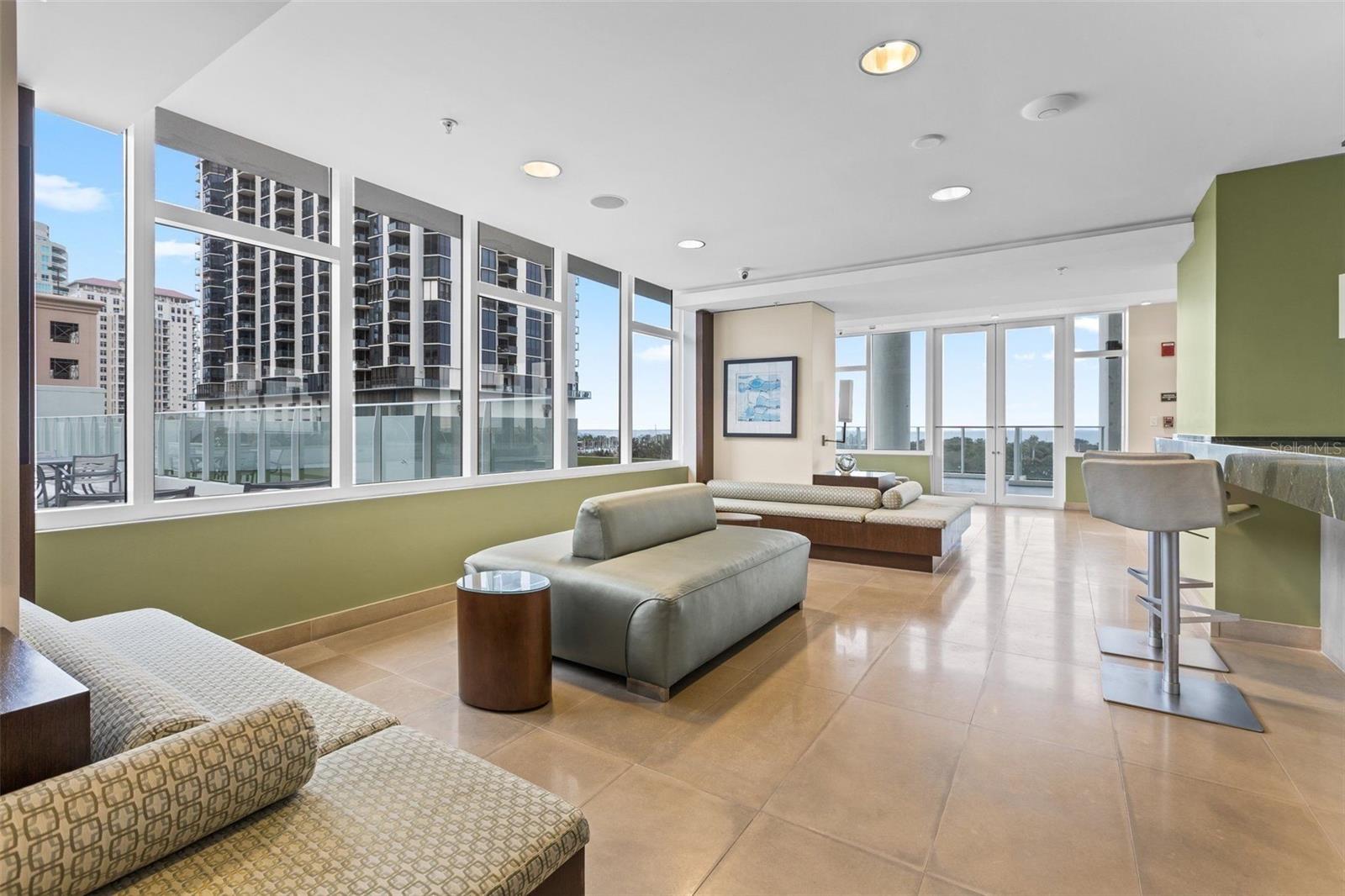 Furnished lounge with floor-to-ceiling windows overlooking nearby high-rise buildings.