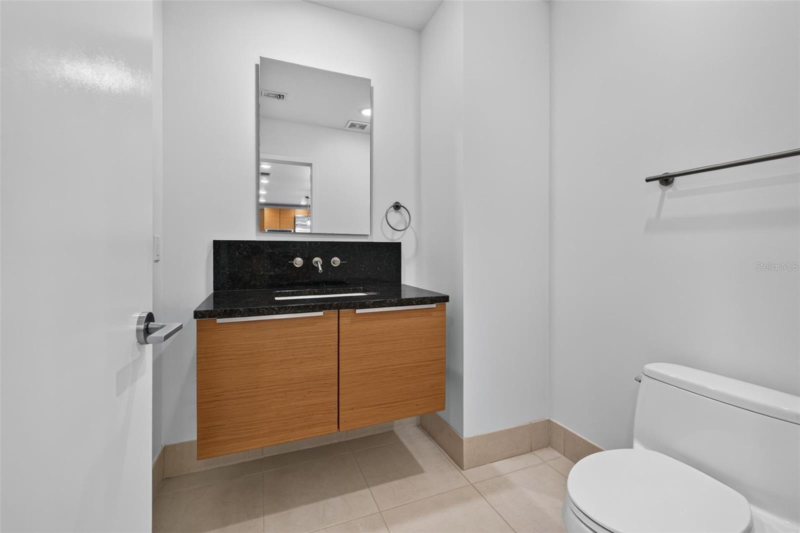 Bathroom with a floating wood vanity, black countertop, and toilet.