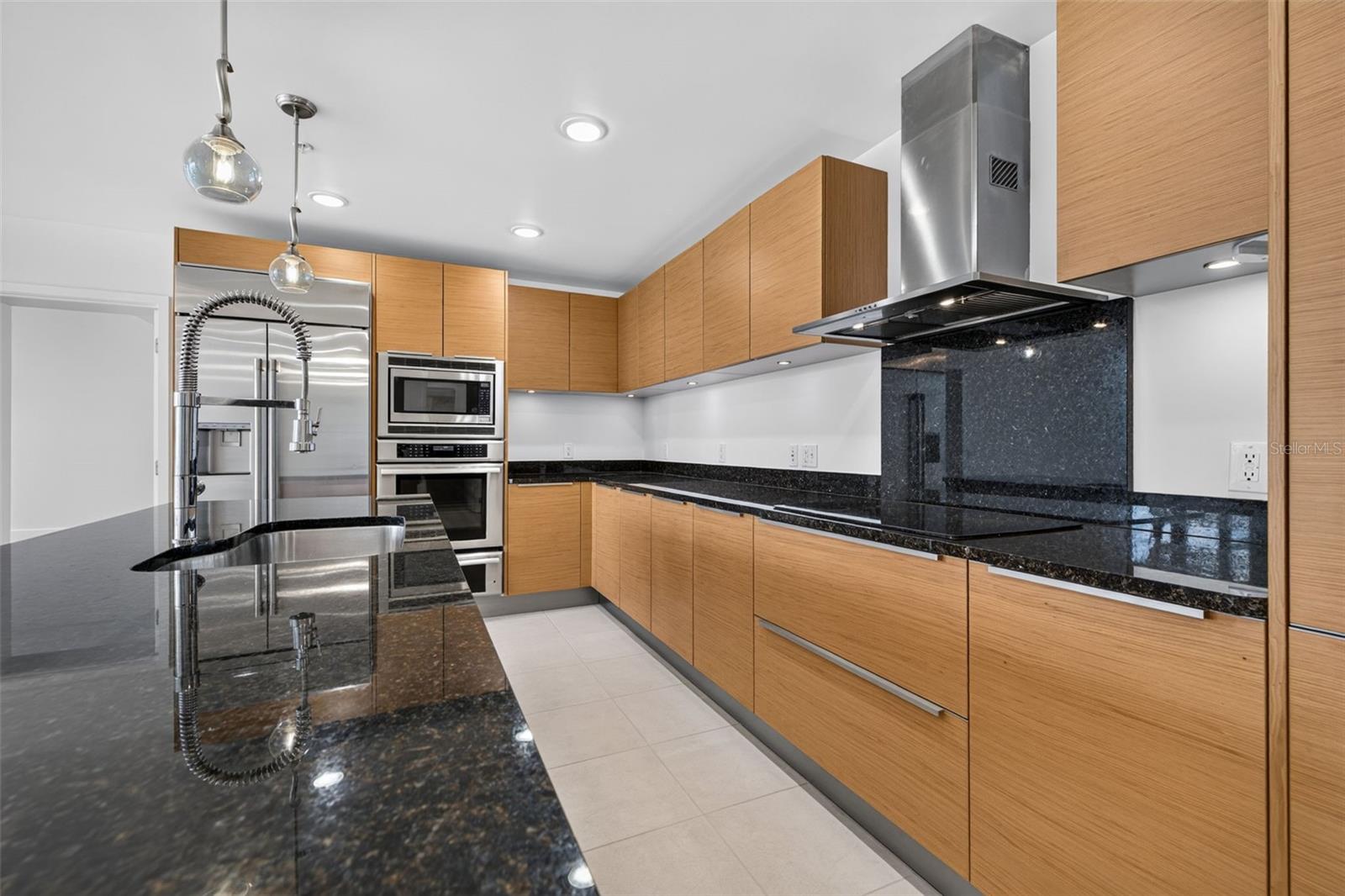 Modern kitchen with light wood cabinets, black stone counters, stainless appliances, and a large island faucet.