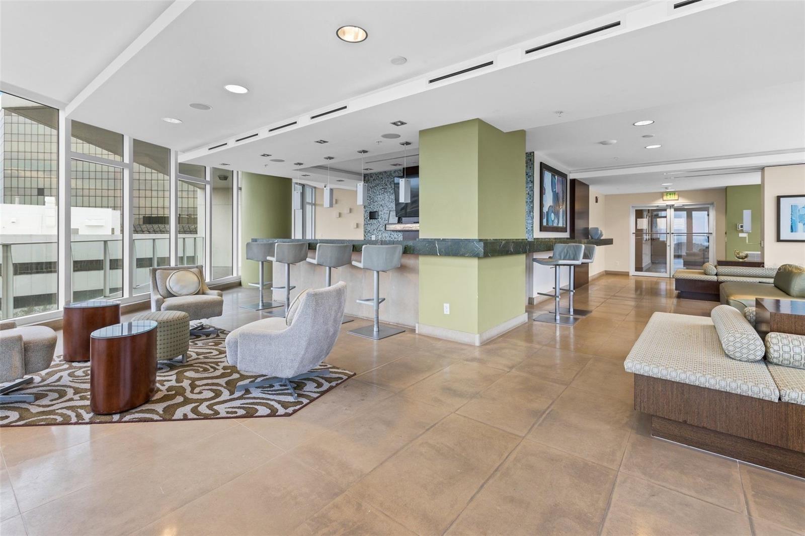 Condominium lounge with a bar counter, lounge seating, and large windows.