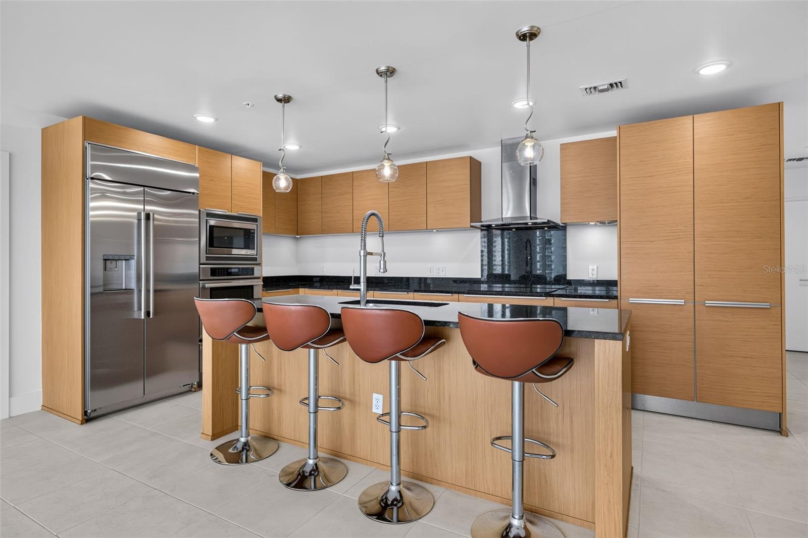 Modern kitchen with wood cabinets, stainless appliances, and an island lined with four brown stools.