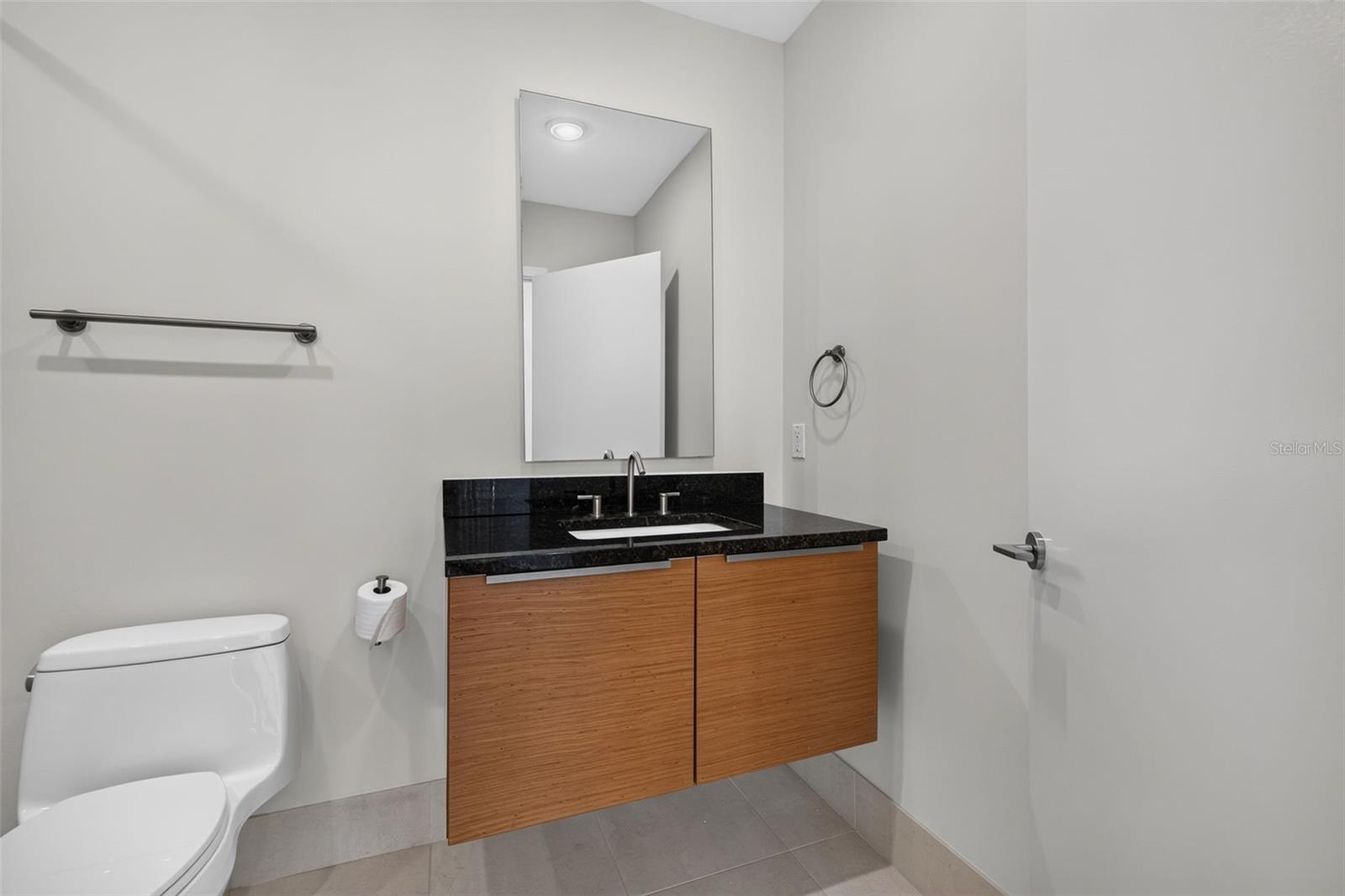 Bathroom with a floating wood vanity, black countertop, large mirror, and white toilet.