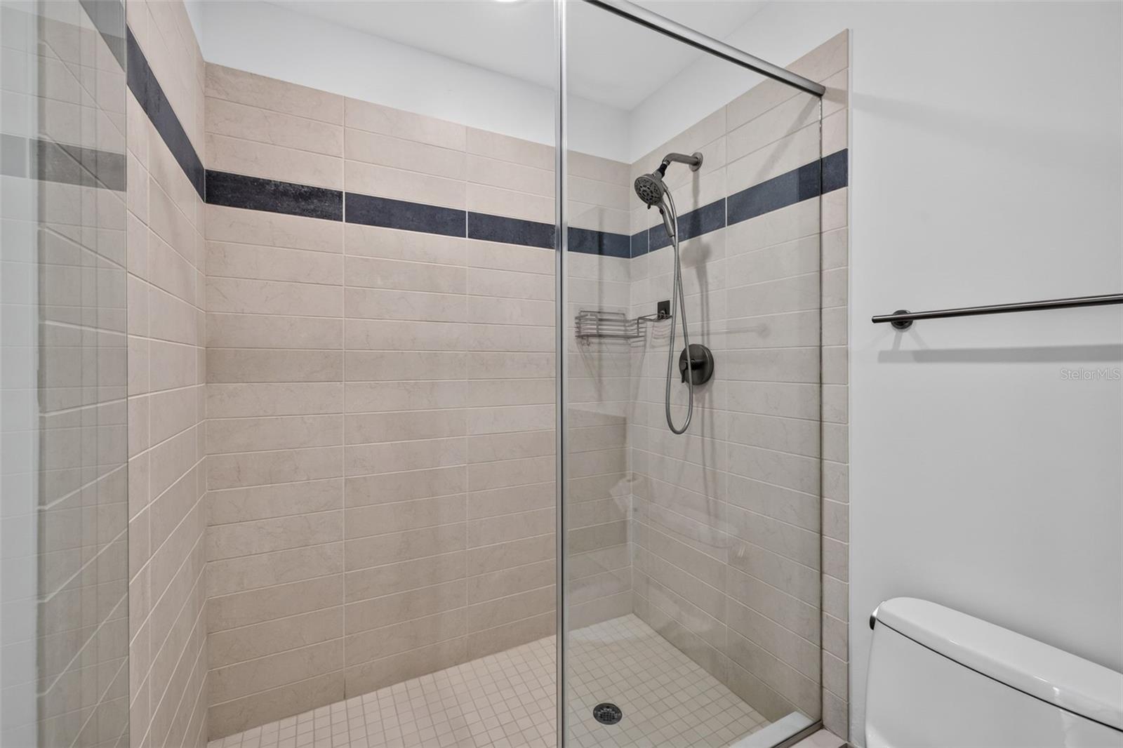 Bathroom shower with a glass enclosure, beige tiles, and a dark accent stripe.