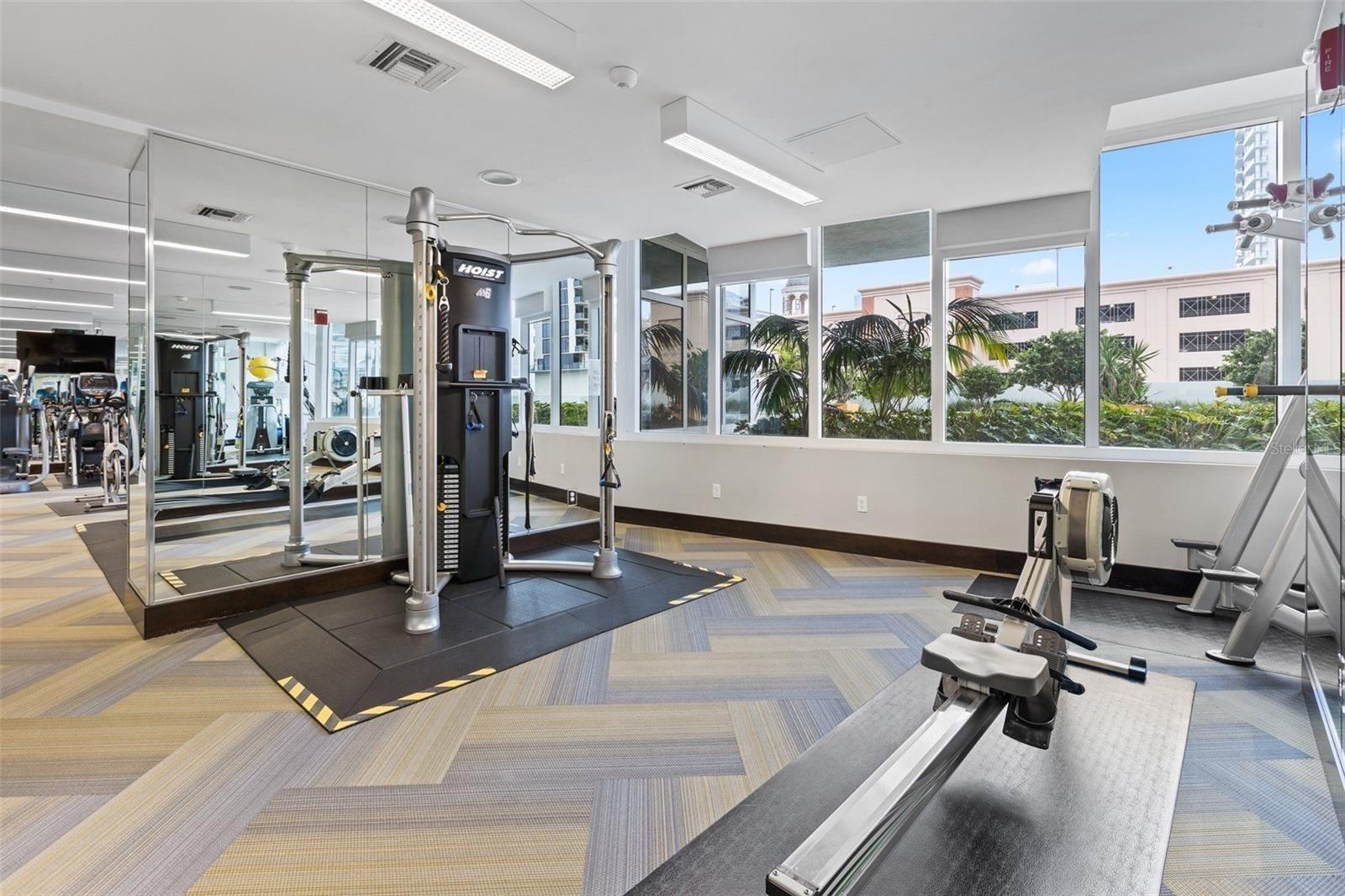Fitness room with weight machines, cardio equipment, mirrored walls, and large windows.