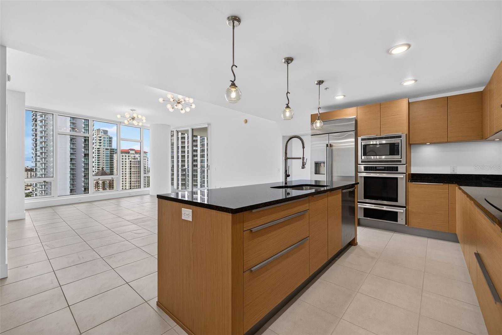 Modern condo kitchen with a wood-and-stone island and large windows overlooking downtown buildings.