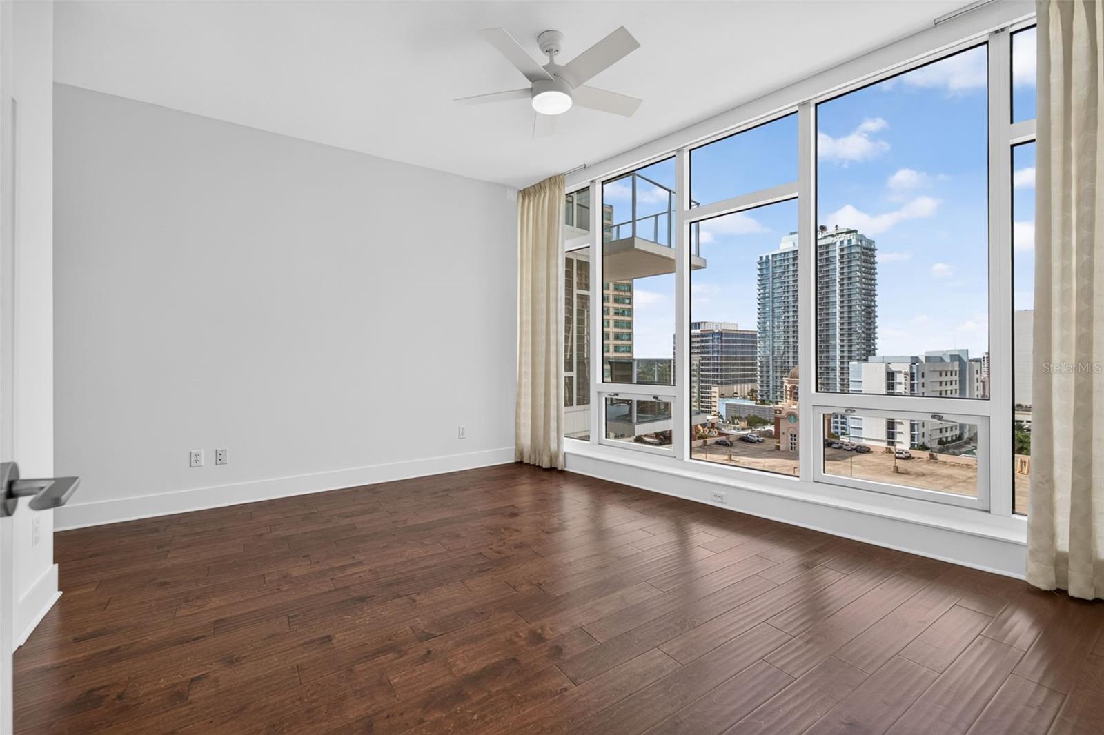 Vacant condo room with dark wood floors and floor-to-ceiling windows overlooking downtown St. Petersburg.
