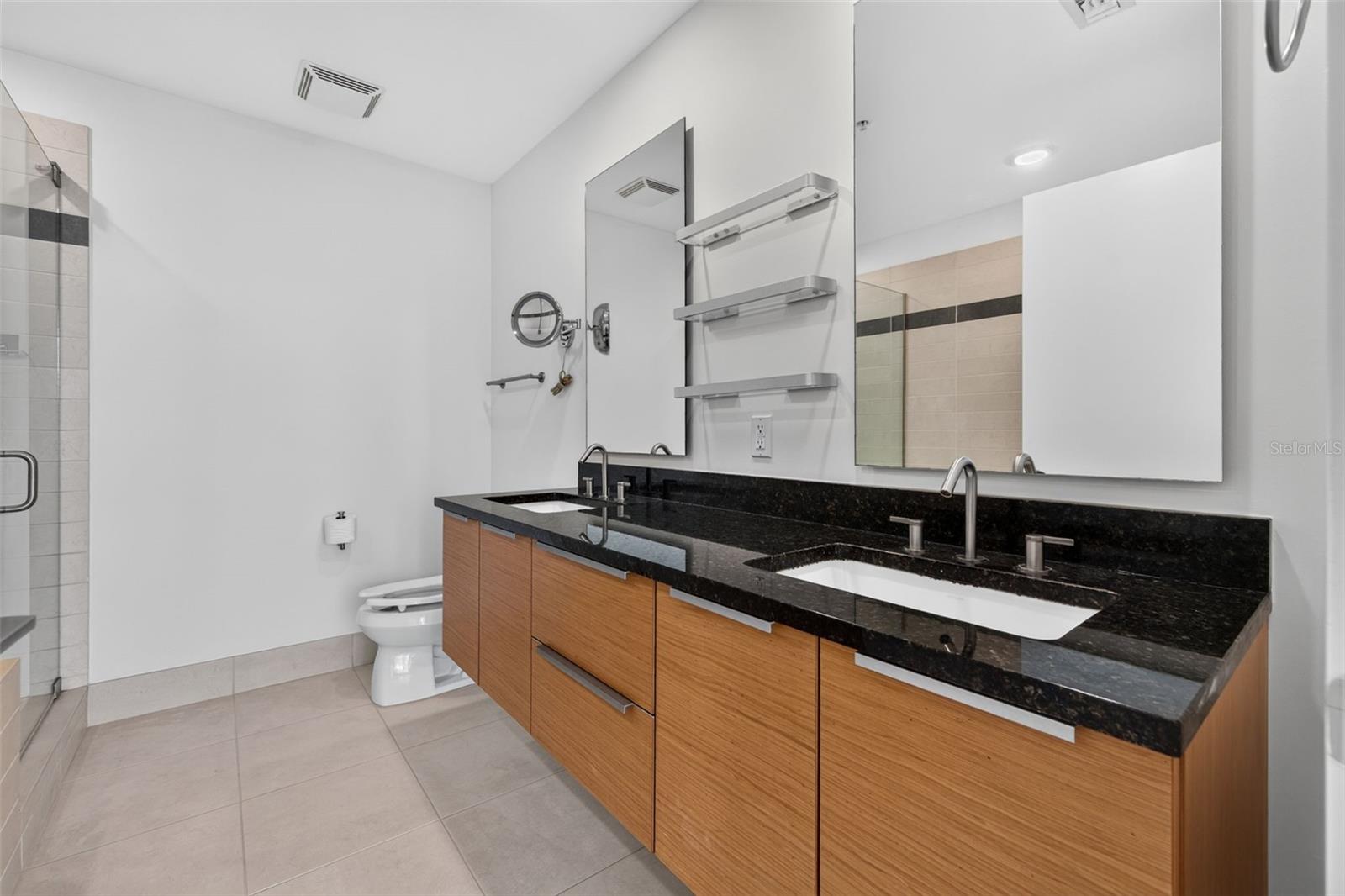 Modern bathroom with a double-sink black stone vanity, wood cabinetry, and glass shower.