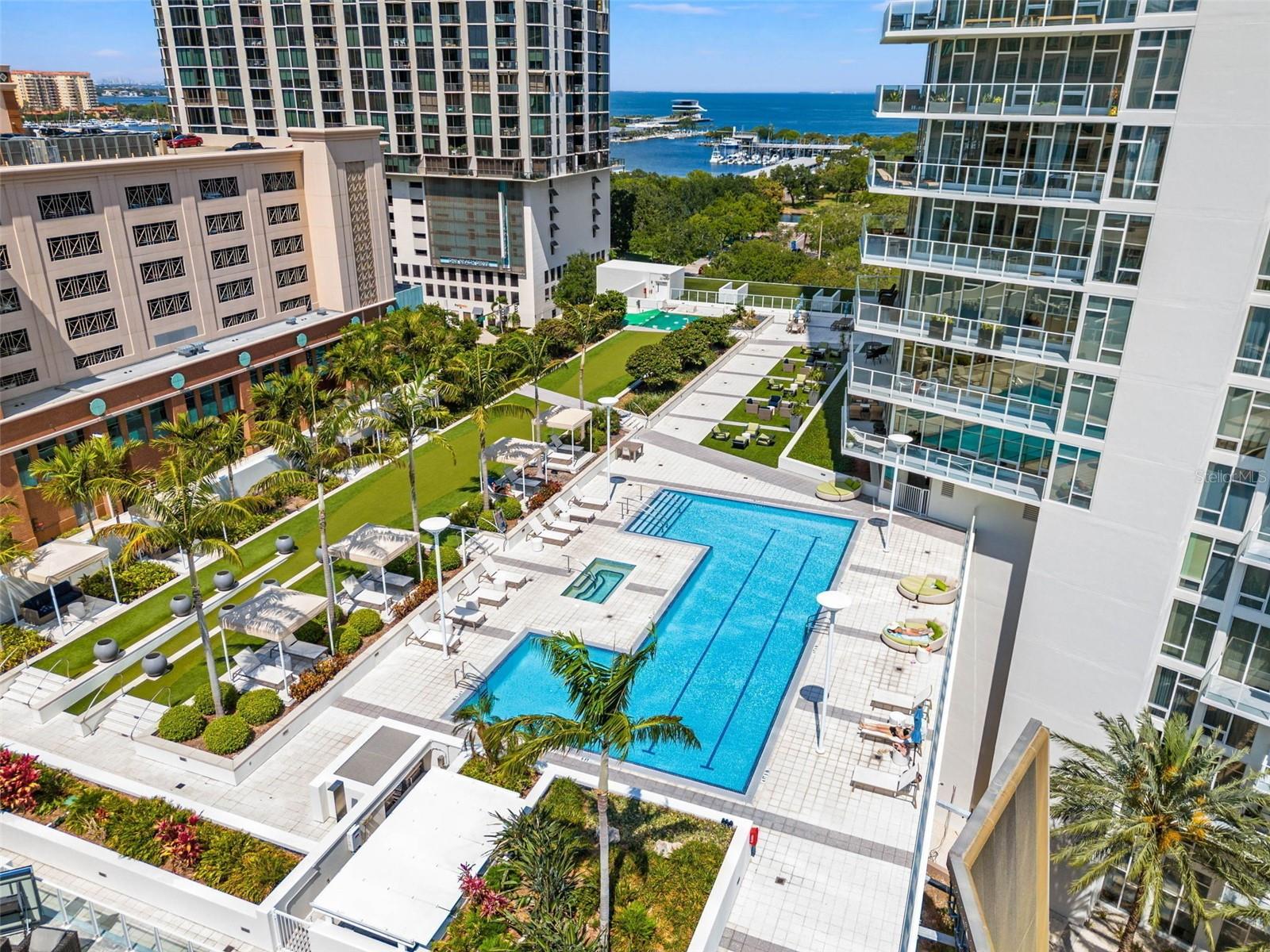 High-rise condominium pool deck with palm trees and seating, overlooking a marina and open water.