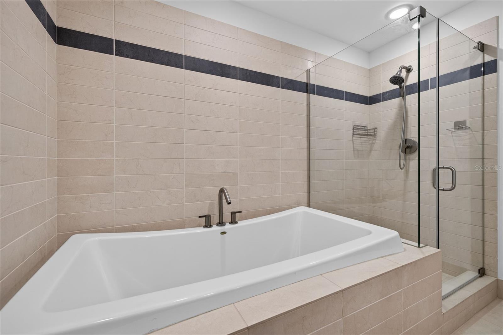 Bathroom with a large soaking tub and glass-enclosed shower, finished in beige tile.