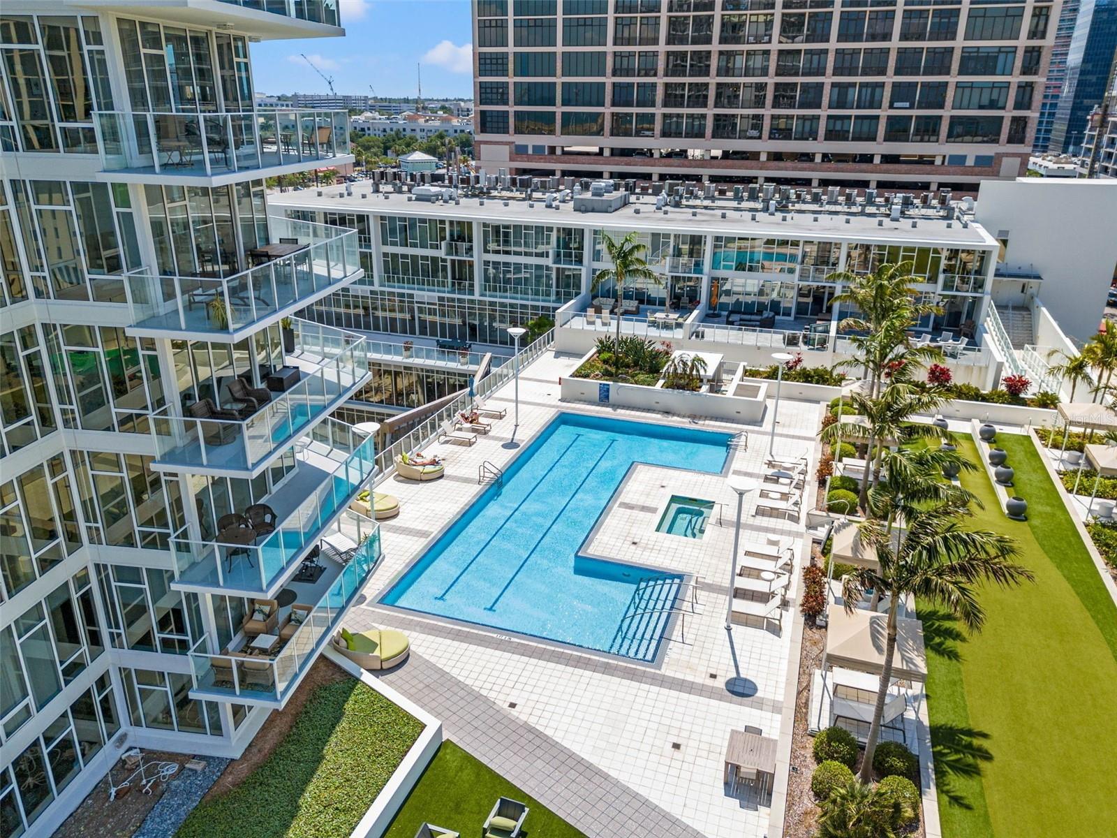 Condominium courtyard pool with a tiled deck, palm trees, and surrounding glass-fronted buildings.