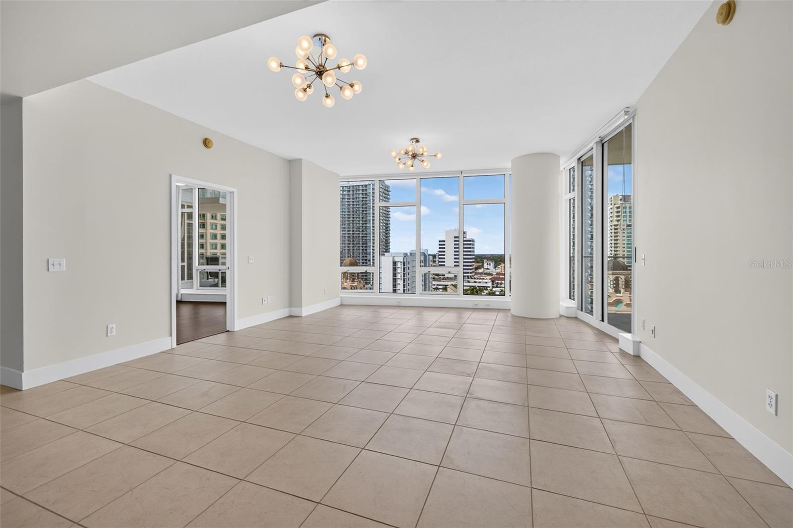 Vacant condo living room with large tile floors, contemporary chandeliers, and expansive downtown views.