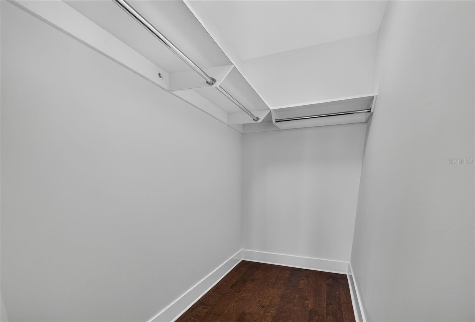 Empty walk-in closet with overhead shelves, hanging rods, and dark wood flooring.