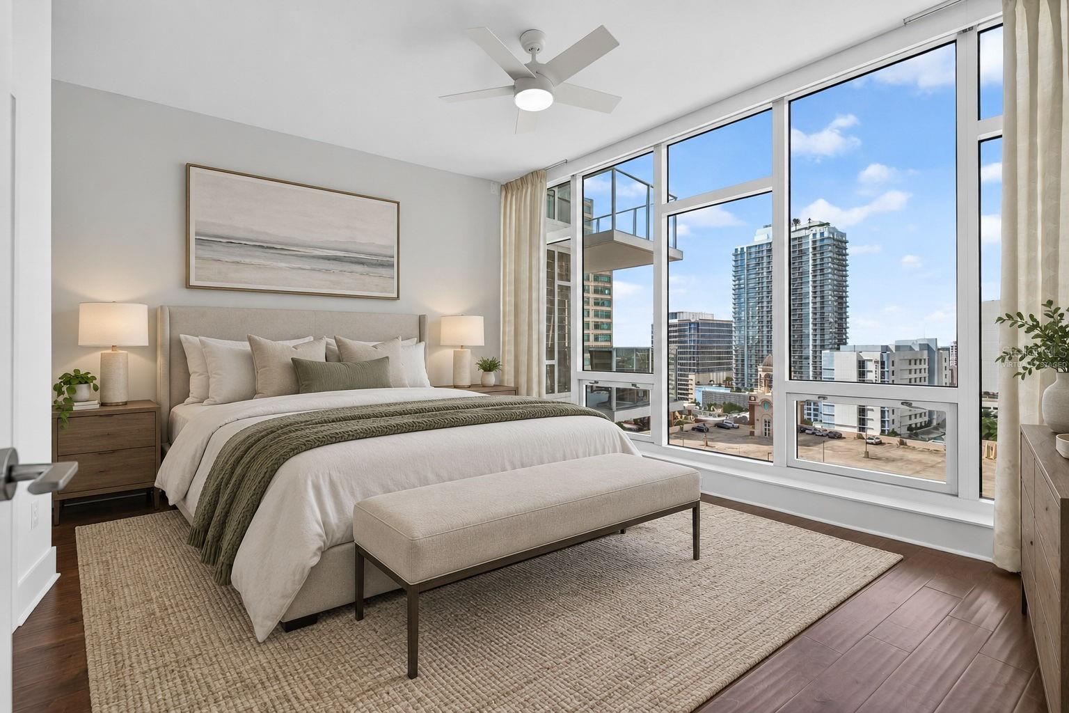 Staged condo bedroom with floor-to-ceiling windows overlooking downtown buildings.