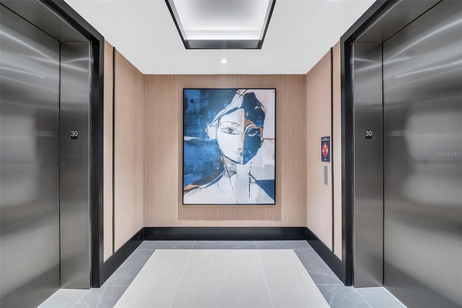 Elevator lobby with stainless steel doors, wood-paneled walls, and large abstract artwork.