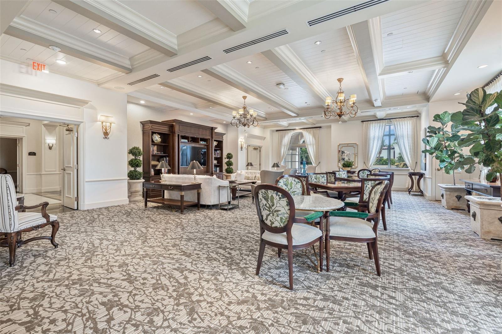 Furnished condominium lounge and dining area with chandeliers, patterned carpet, and tall windows.