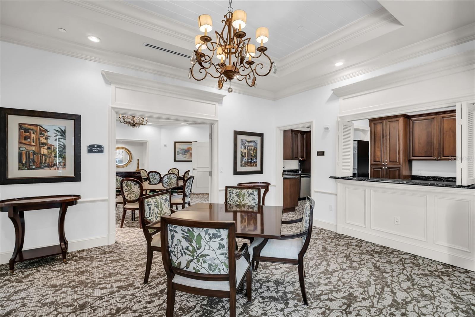 Dining room with a dark wood table, floral-upholstered chairs, ornate chandelier, and kitchen pass-through.
