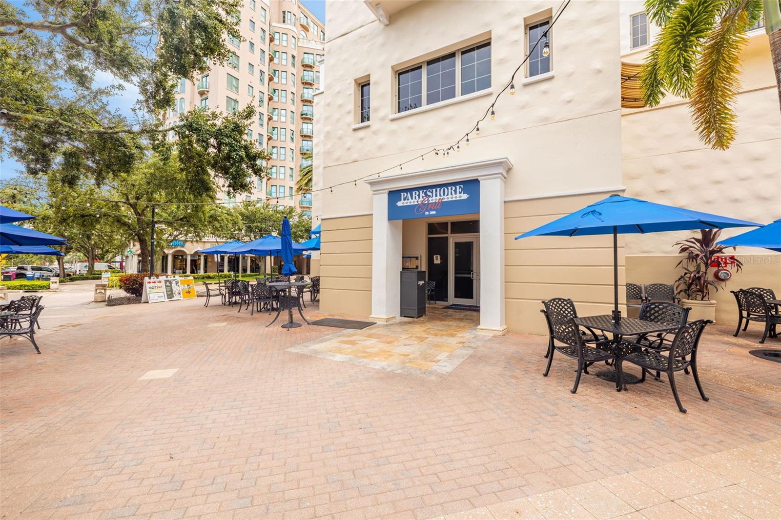 Parkshore Grill entrance beside an outdoor patio with black tables and bright blue umbrellas.