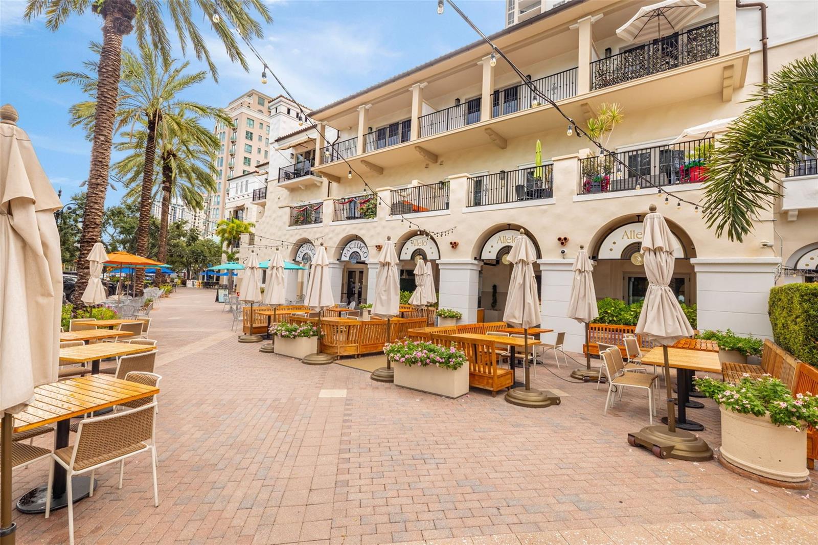 Building courtyard with arched storefronts, balconies, palm trees, and café seating.