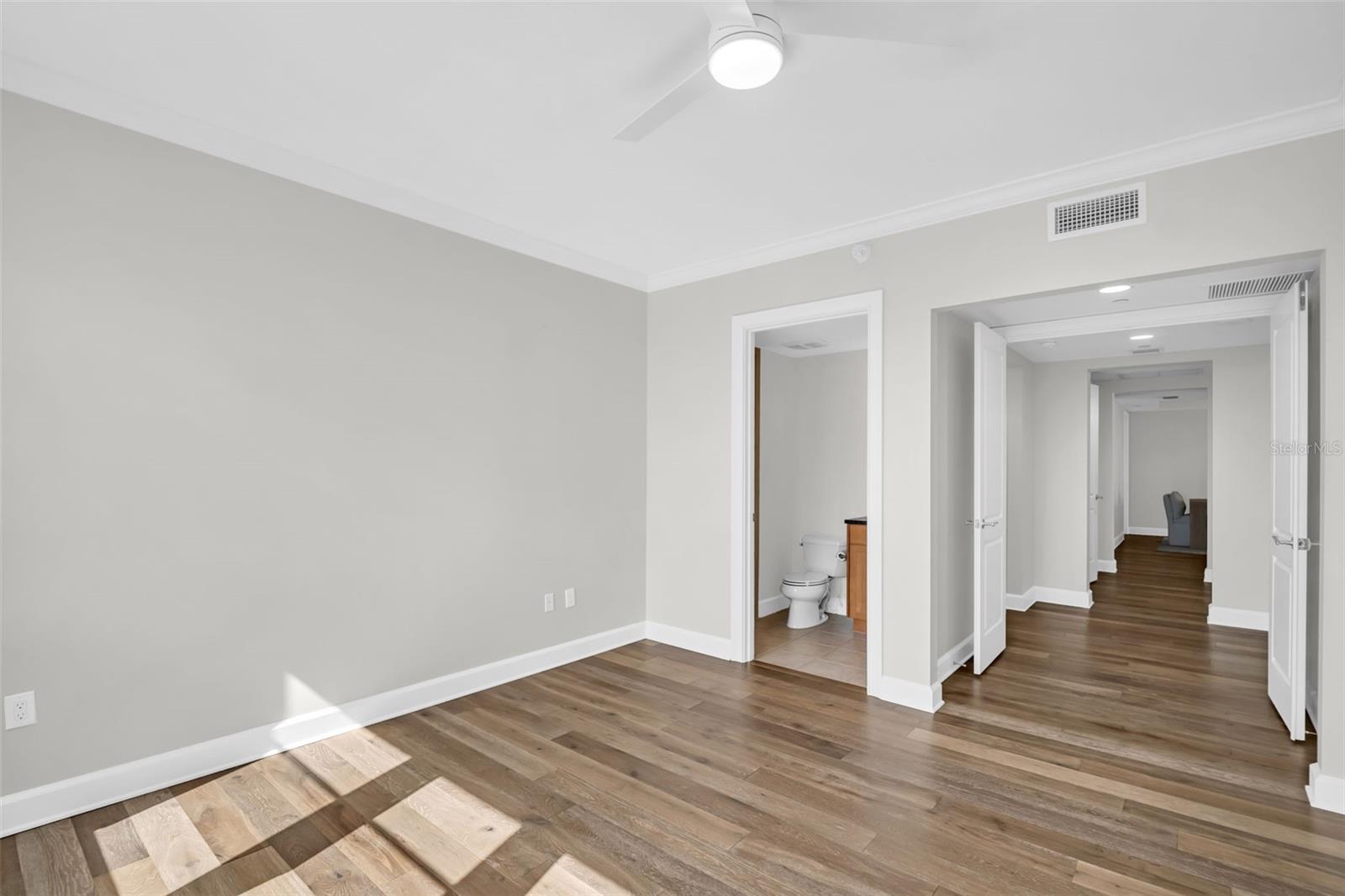 Empty room with wood-look floors, ceiling fan, and open bathroom and hallway doorways.