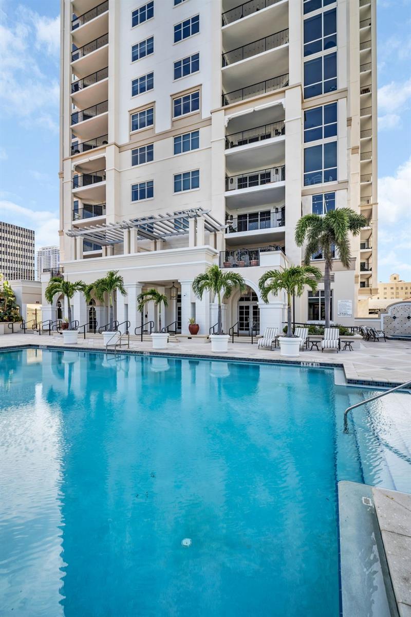 Condominium pool with palm trees and lounge chairs beneath the building’s balconies.