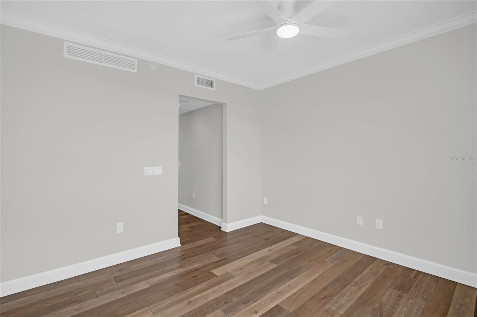 Empty room with wide-plank wood flooring, gray walls, and a white ceiling fan.