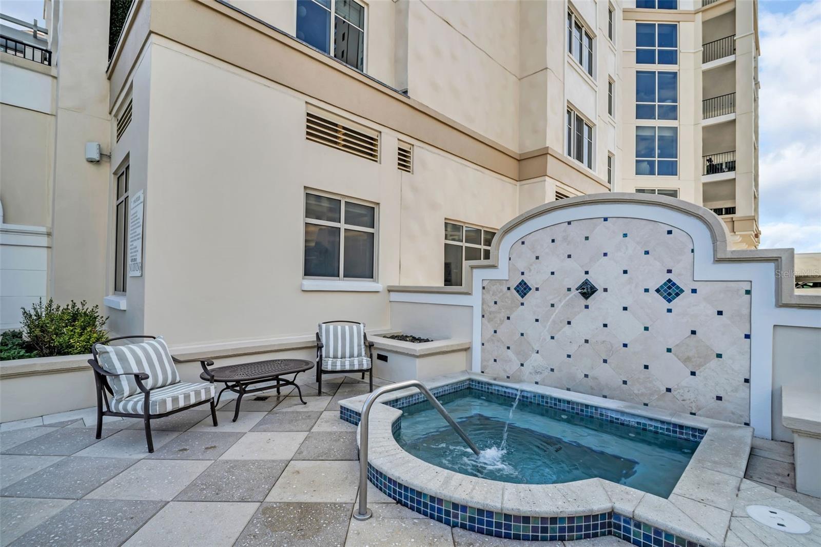 Courtyard spa beside a condominium, with a tiled wall and striped patio seating.