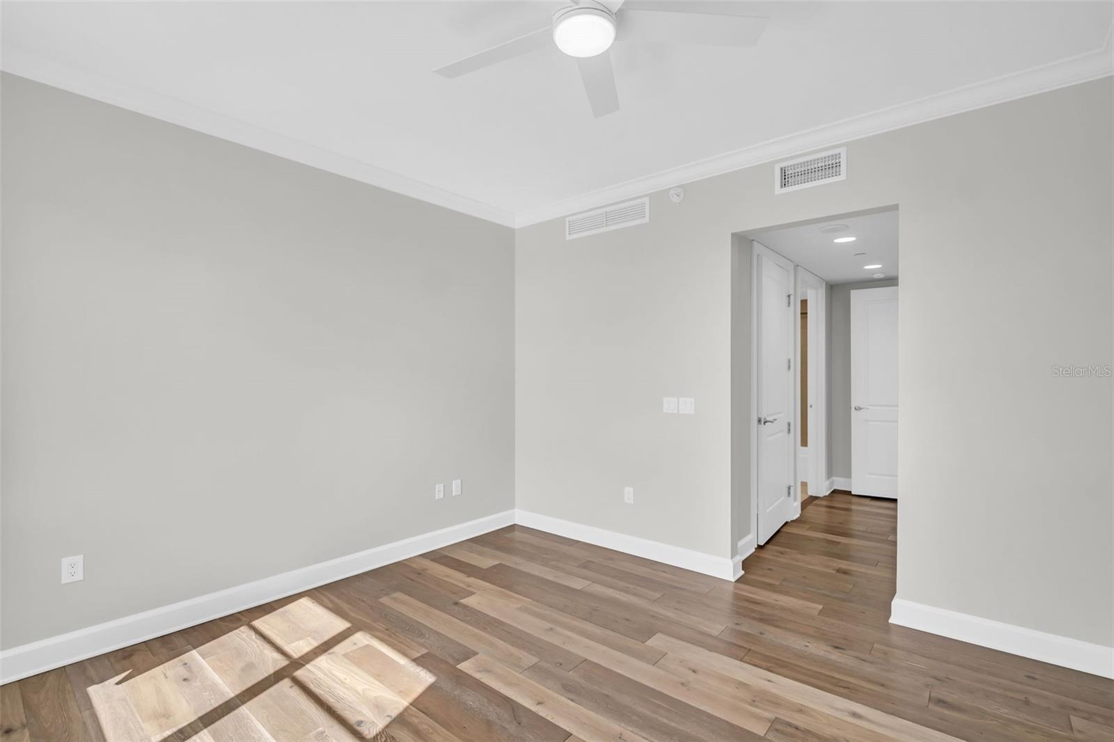 Empty room with wide-plank wood flooring, a ceiling fan, and an open hallway doorway.