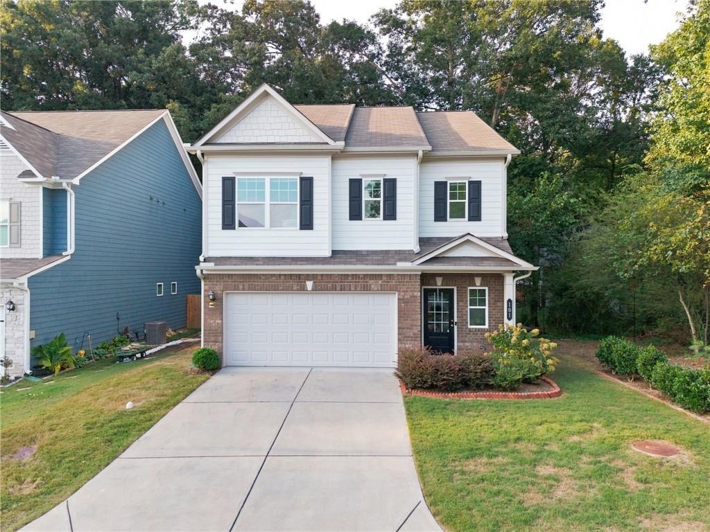 Two-story white-and-brick house with black shutters, an attached garage, and a wide concrete driveway.