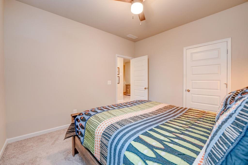 Bedroom with a colorful striped quilt, beige walls, ceiling fan, and open doorway.