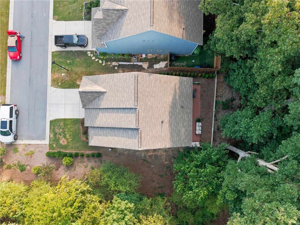 Aerial view of a house beside a street, surrounded by mature trees and greenery.