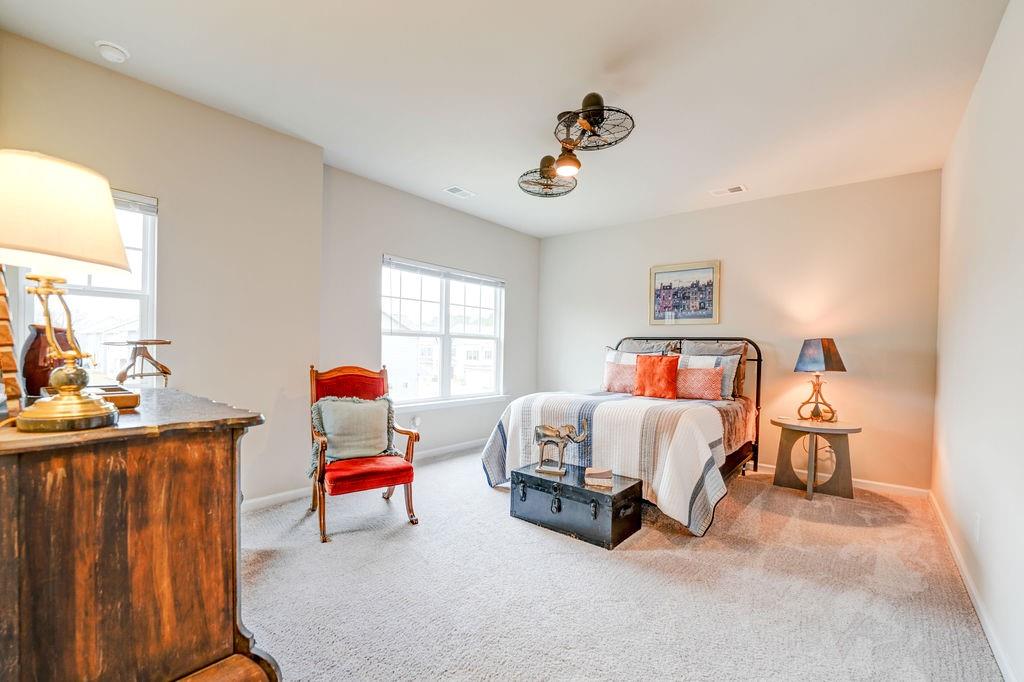Furnished bedroom with orange accent pillows, a red chair, and two bright windows.